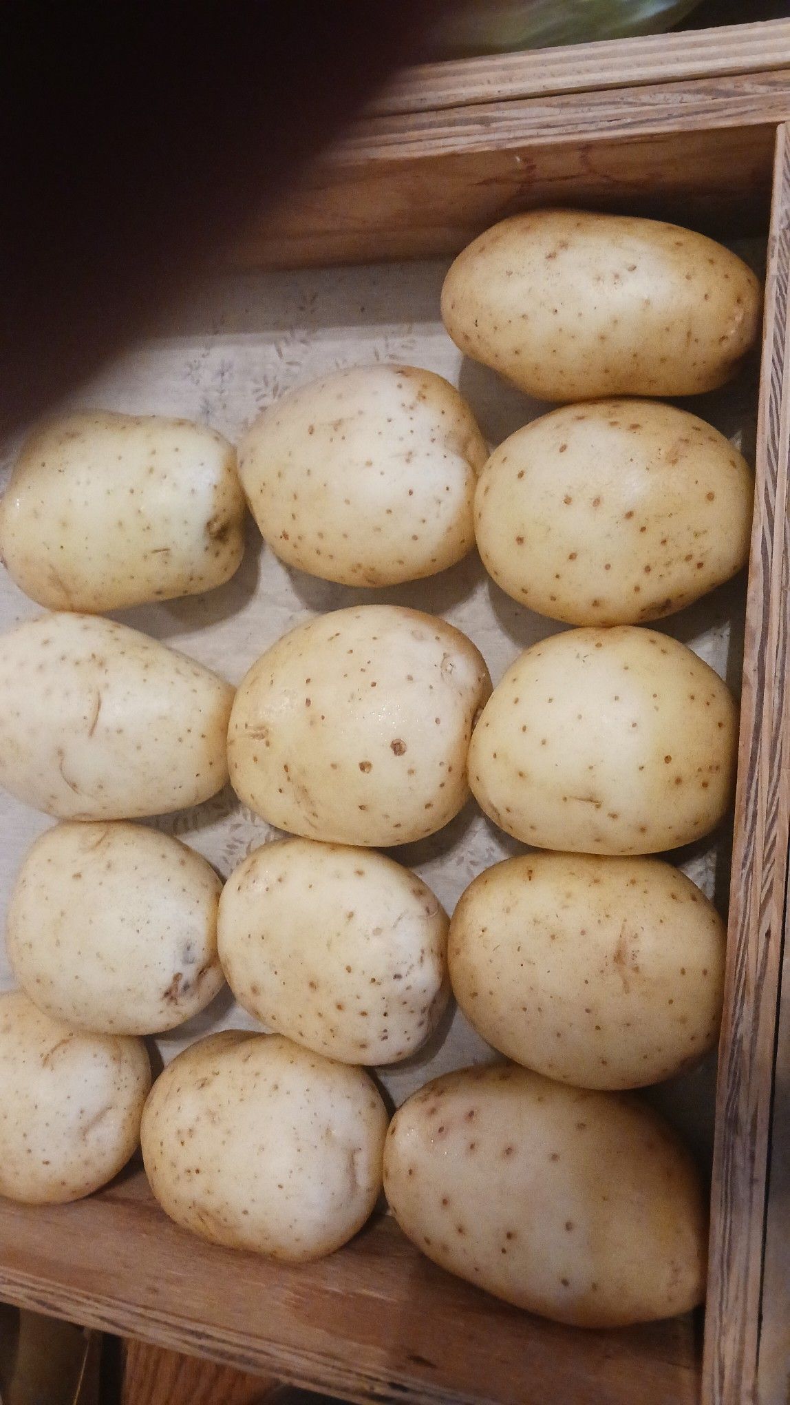 Potatoes in a wooden box; off-white with brown spots.