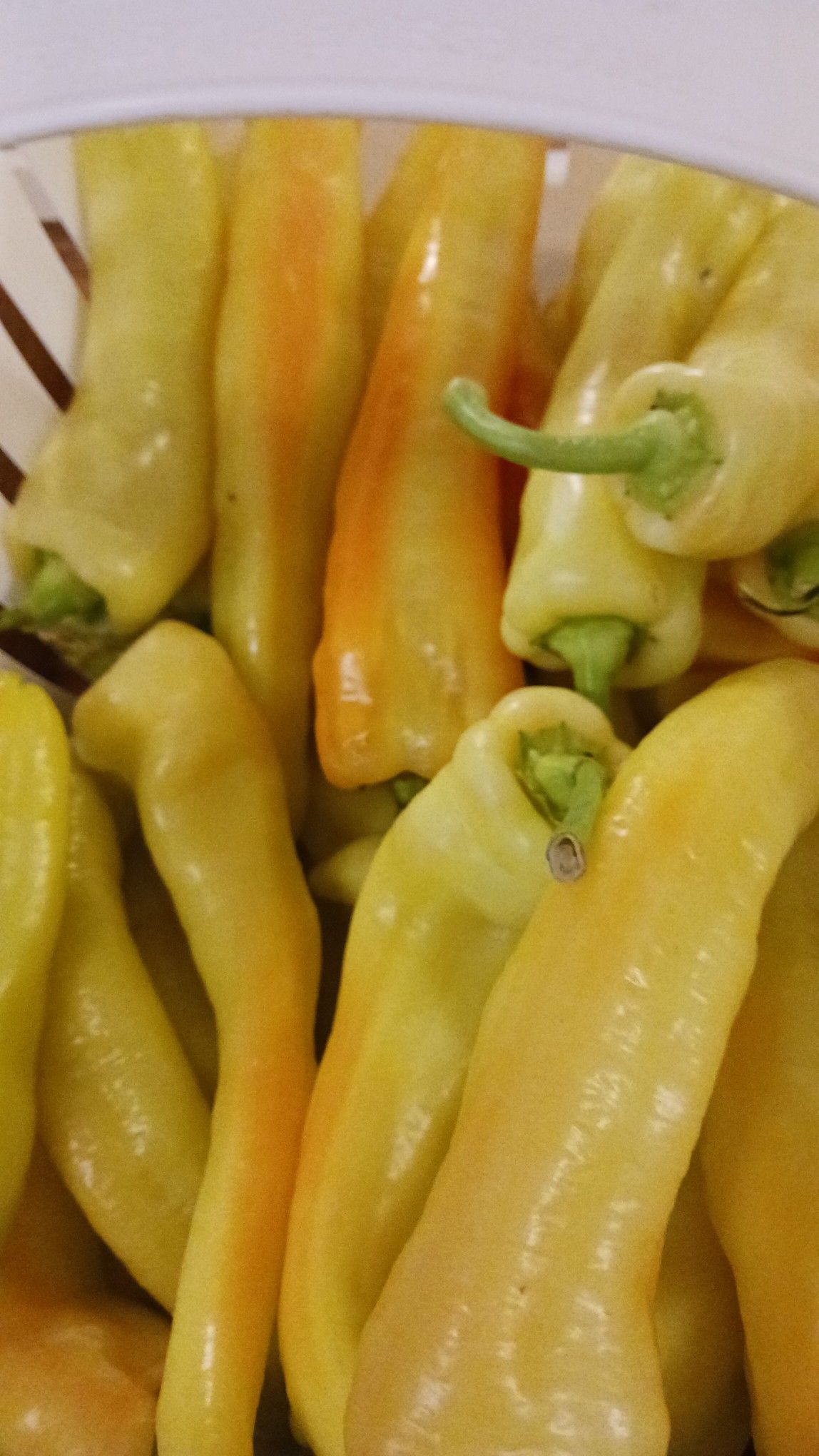 Close-up of a white basket filled with yellow banana peppers, some with orange blush.