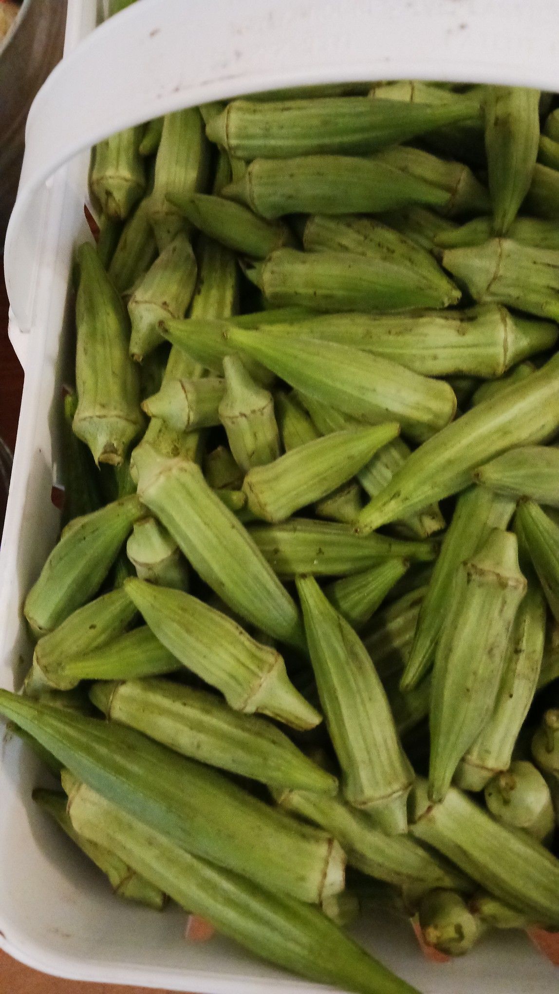 Green okra pods in a white basket, close-up shot.