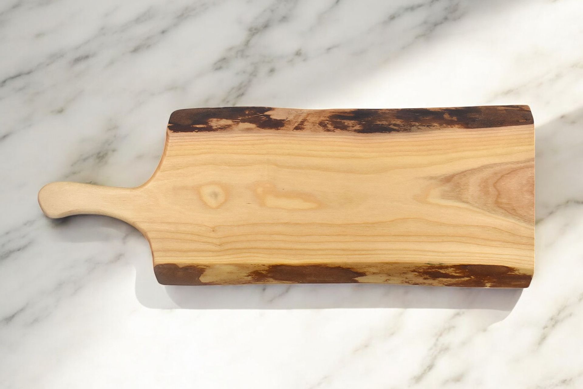 A wooden cutting board with a handle on a marble surface
