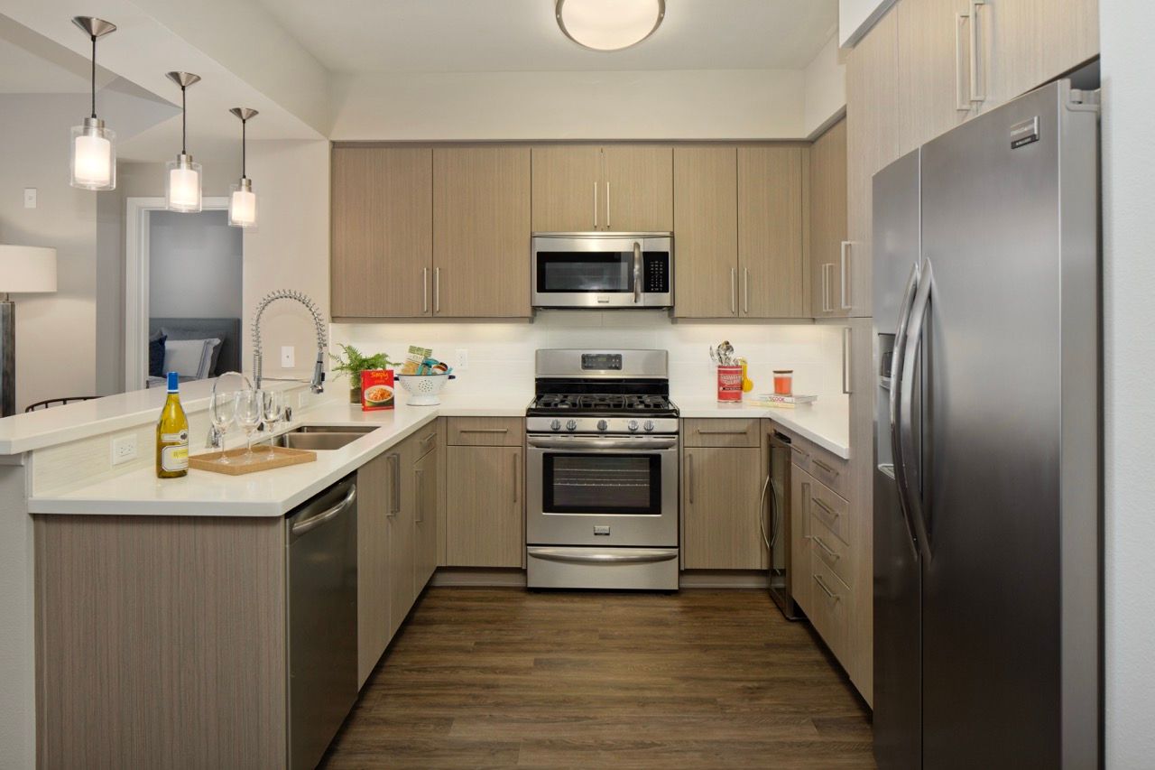 Modern apartment kitchen with an island, stainless steel appliances, and wood-tone cabinets.
