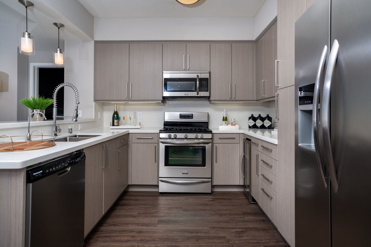 Modern apartment kitchen with stainless steel appliances, gray wood cabinets, and a double sink.