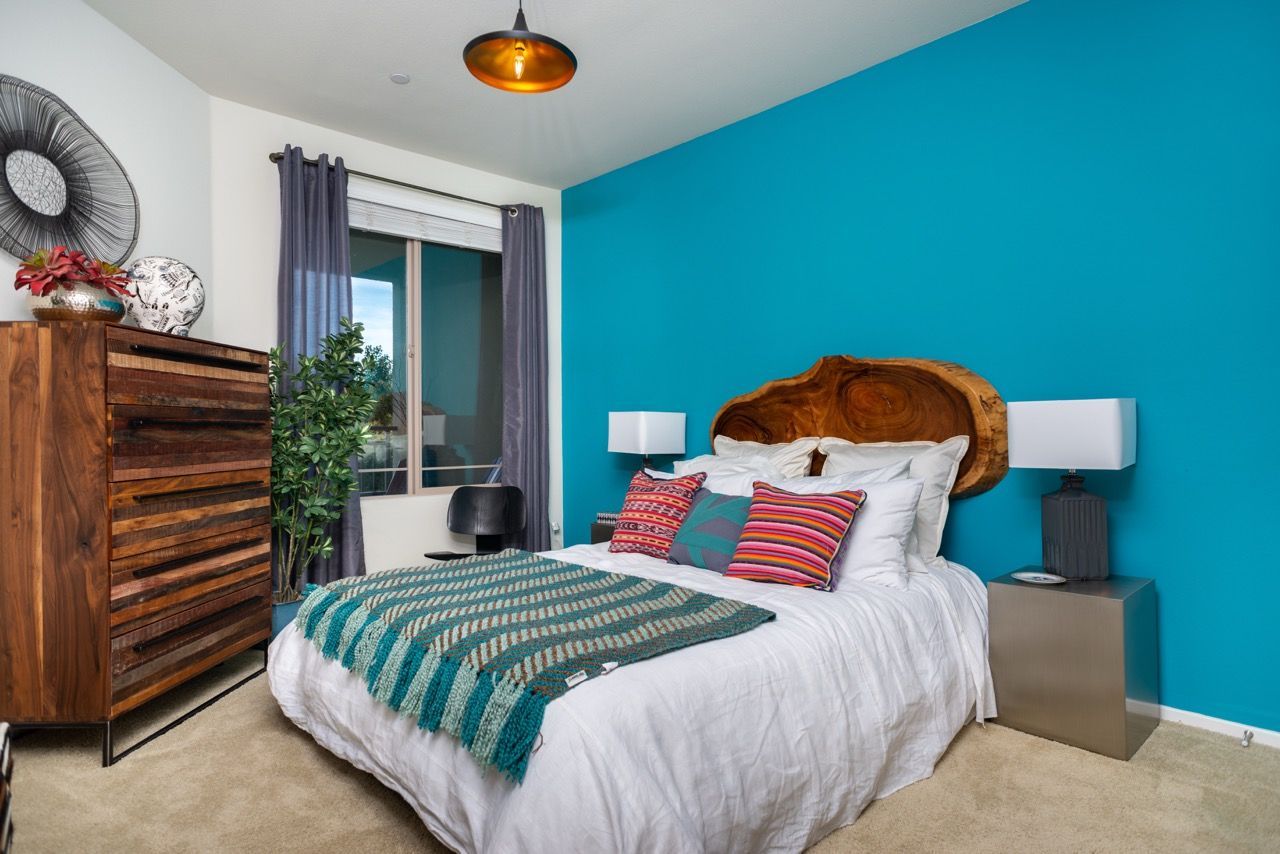 Bedroom in an apartment with teal accent wall, bed, dresser, and colorful pillows.