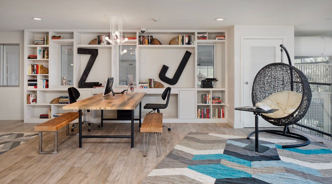 Modern apartment office area with a wooden desk, built-in shelves, and a hanging chair by a window.