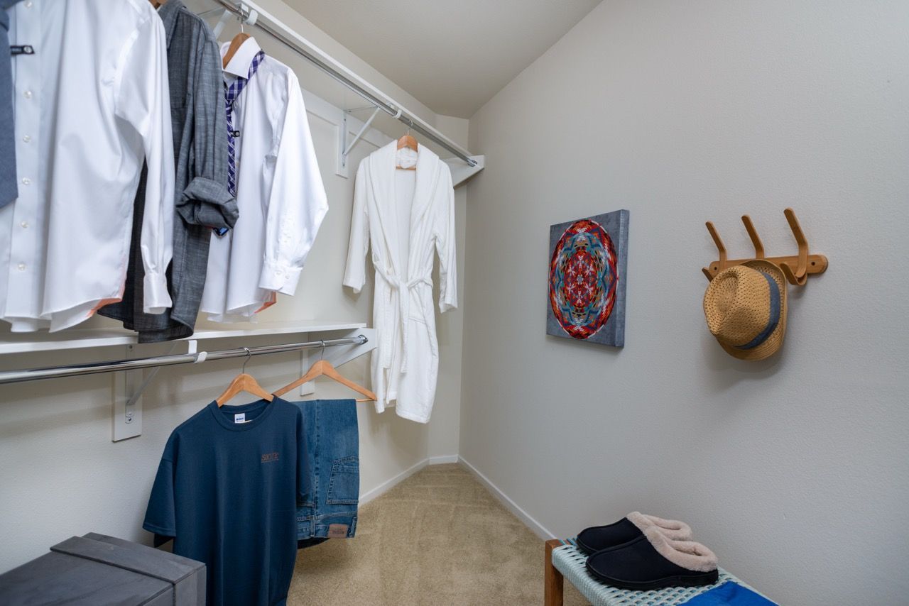 Walk-in closet with shirts hanging on rods, a white robe, and a hat on wall hooks.