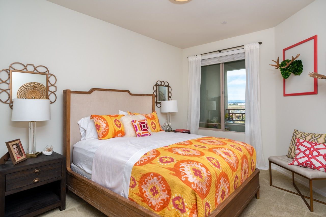Bedroom with a wooden bed, vibrant orange bedding, and a window with white curtains.