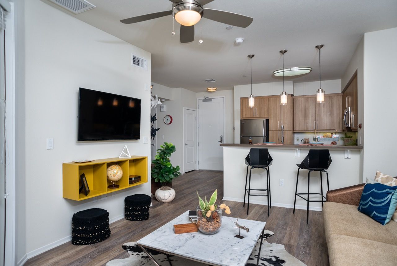 Open-concept living area with wall-mounted TV, yellow cubed shelf, and kitchen island with two stools.