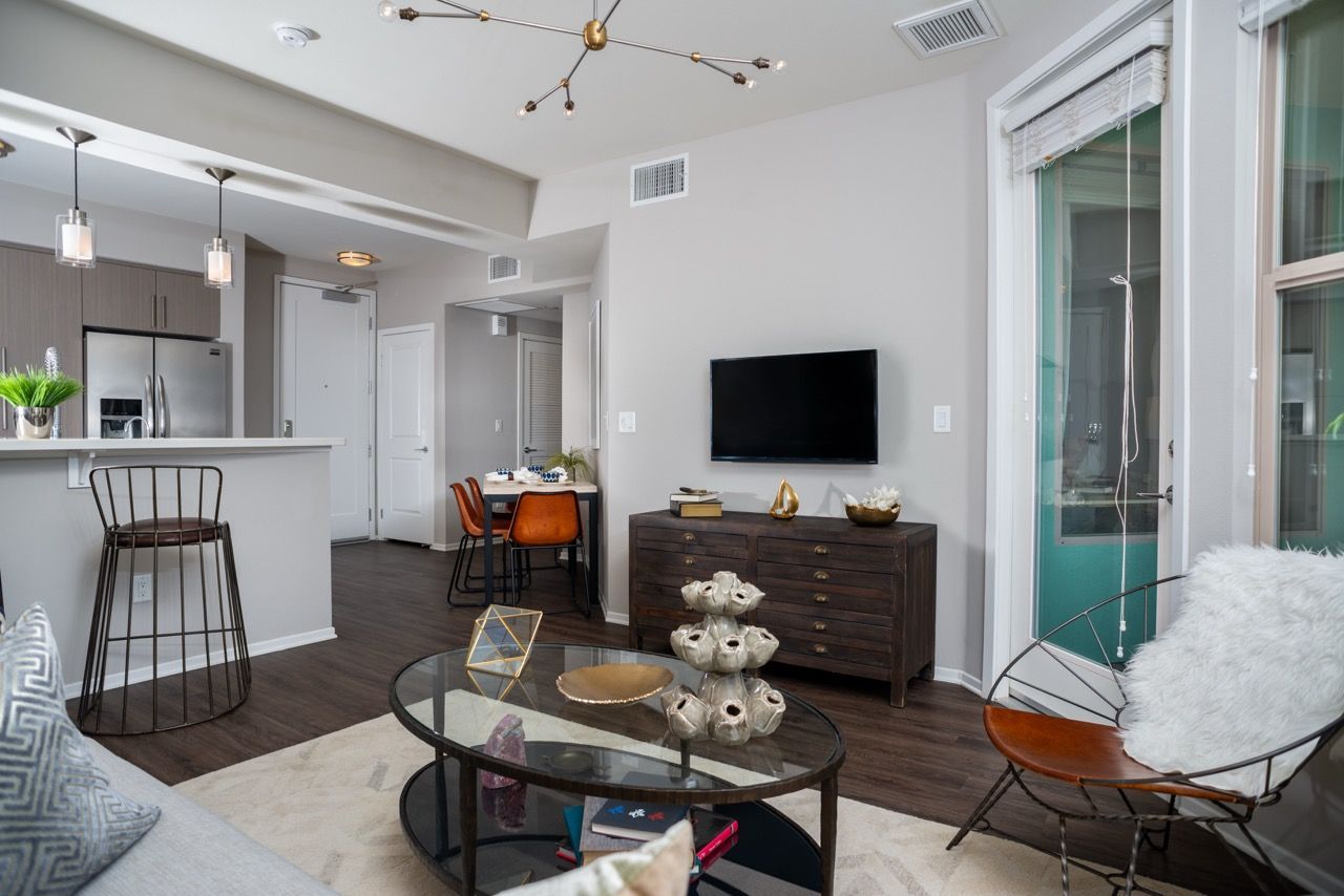 Open-concept living room with TV on wall, glass coffee table, and kitchen island nearby.