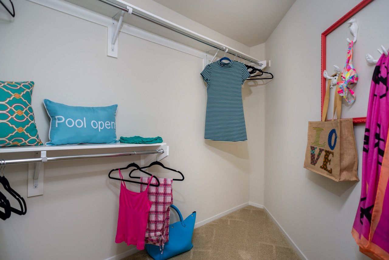 Walk-in closet with shelves, a hanging rod, and colorful clothes and bags.