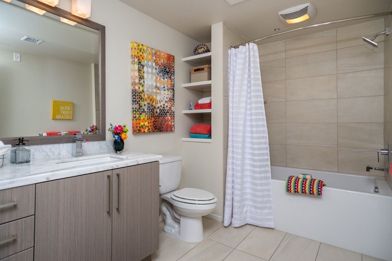 Bathroom in an apartment with a single-sink vanity, toilet, open shelves, and a tub/shower with a white striped curtain.