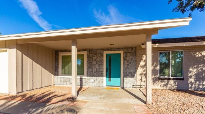 Beige and turquoise mid-century modern home exterior with a turquoise front door and two windows under a carport-style roof.