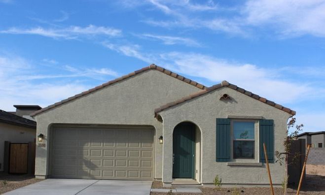 Beige stucco house with a two-car garage, green door and shutters, and a blue sky.