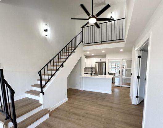 Interior of a modern home with a staircase, loft, and open kitchen; white walls, black railing, light wood floors.