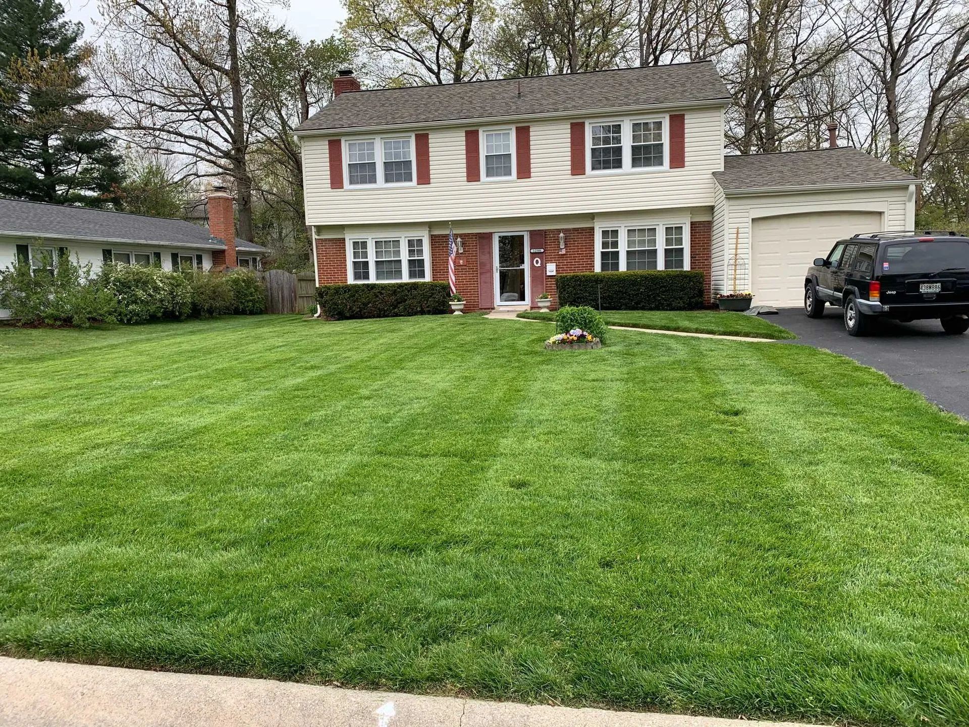 Two-story house with green lawn; SUV in driveway. Red shutters, beige siding, brick facade.