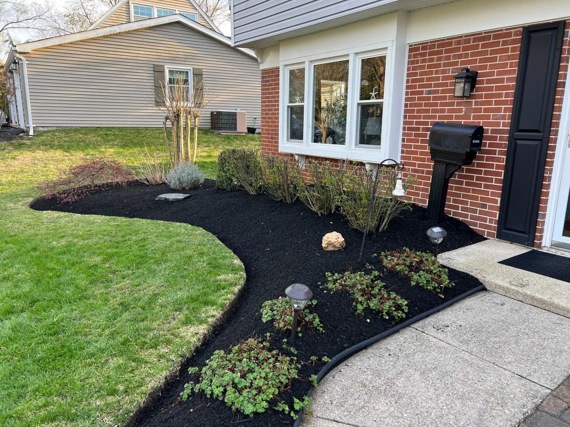 A house with a black mulch flower bed bordering the lawn and walkway. The house has brick
and siding