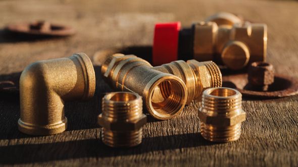 Brass plumbing fittings on a wooden surface; including elbows, couplings, and plugs.