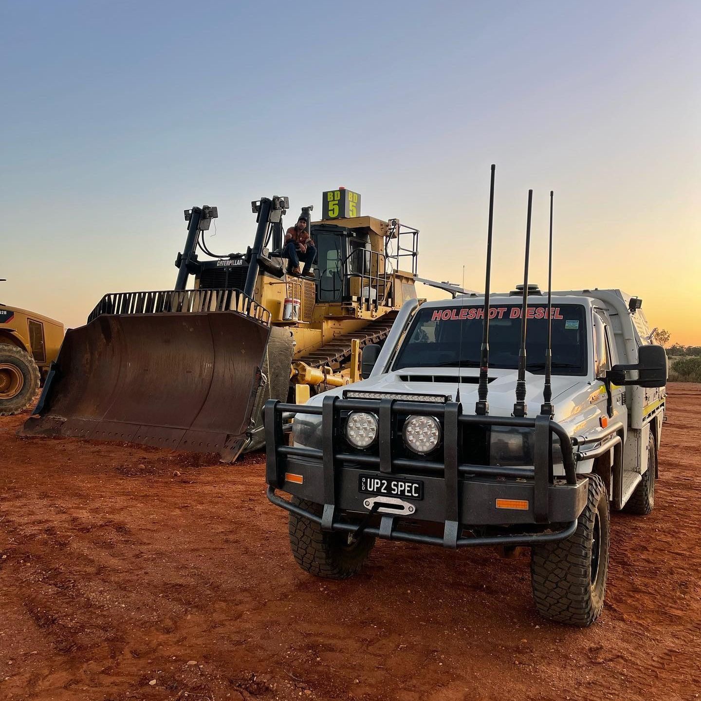 White Truck With Antennas in Front of a Yellow Bulldozer on Red Dirt at Sunset — HOLESHOT Diesel In Gympie, QLD