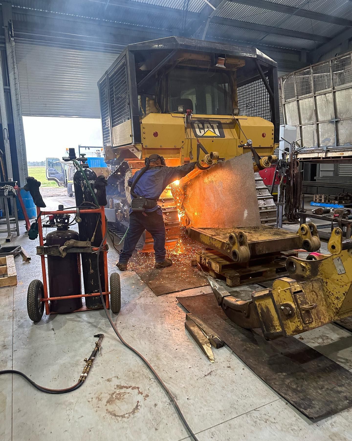 A Person Welds on a Yellow Caterpillar Bulldozer Inside a Metal Building — HOLESHOT Diesel In Emerald, QLD