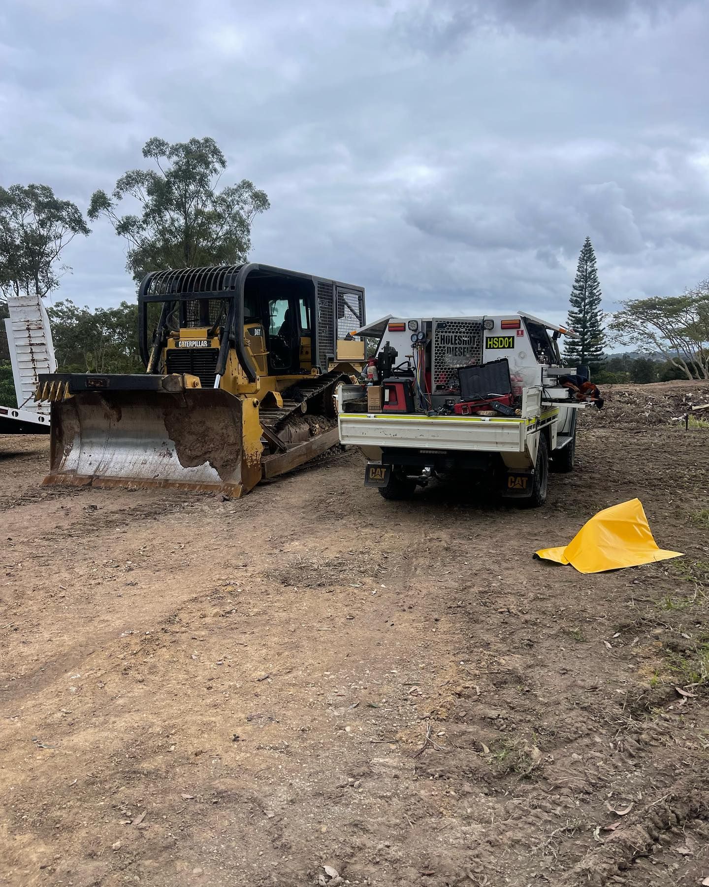 Bulldozer and Utility Truck on Dirt Ground Under Cloudy Sky — HOLESHOT Diesel In Gympie, QLD