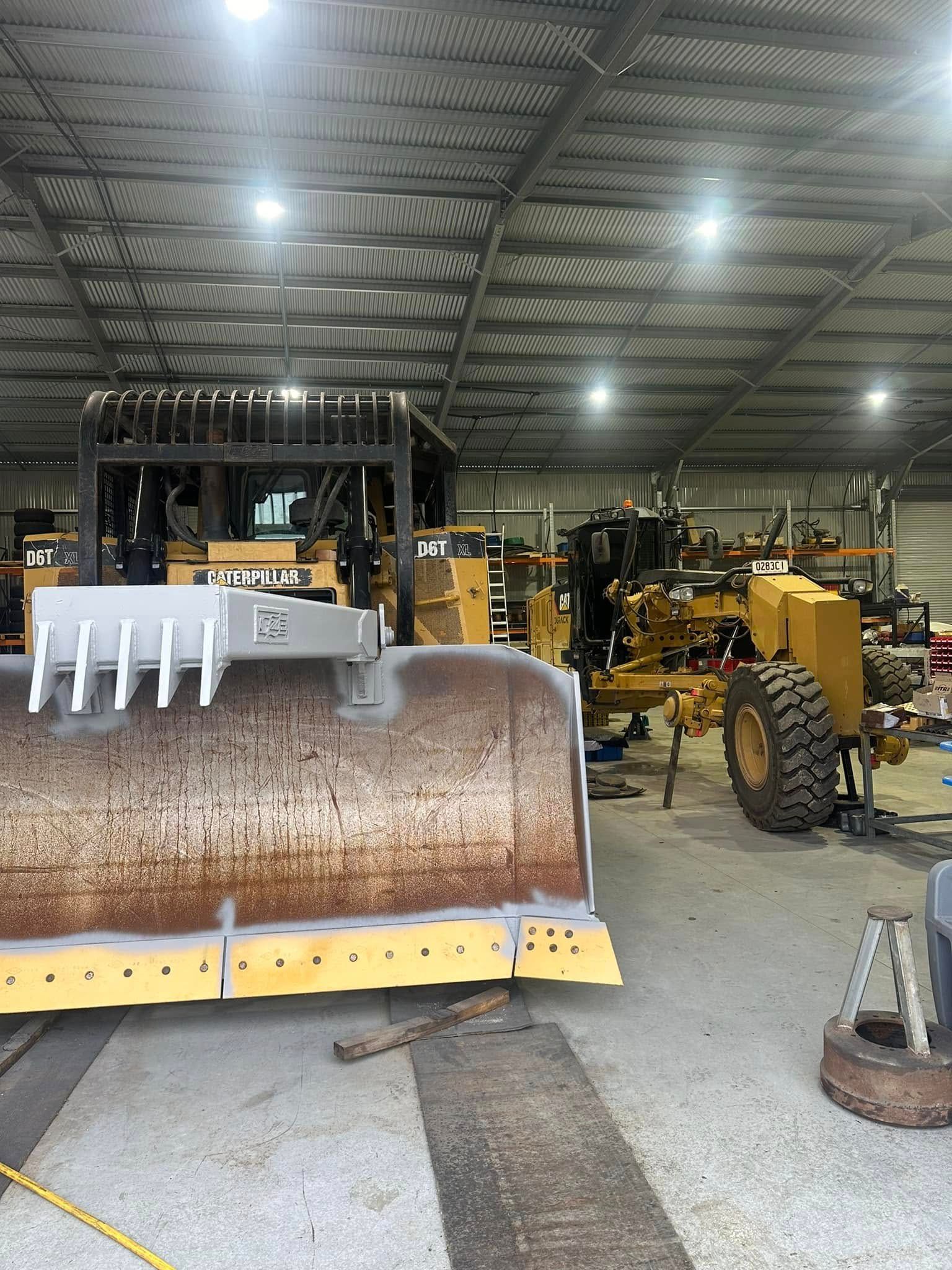 Large Yellow Grader Blade and Grader Inside a Workshop — HOLESHOT Diesel In Emerald, QLD