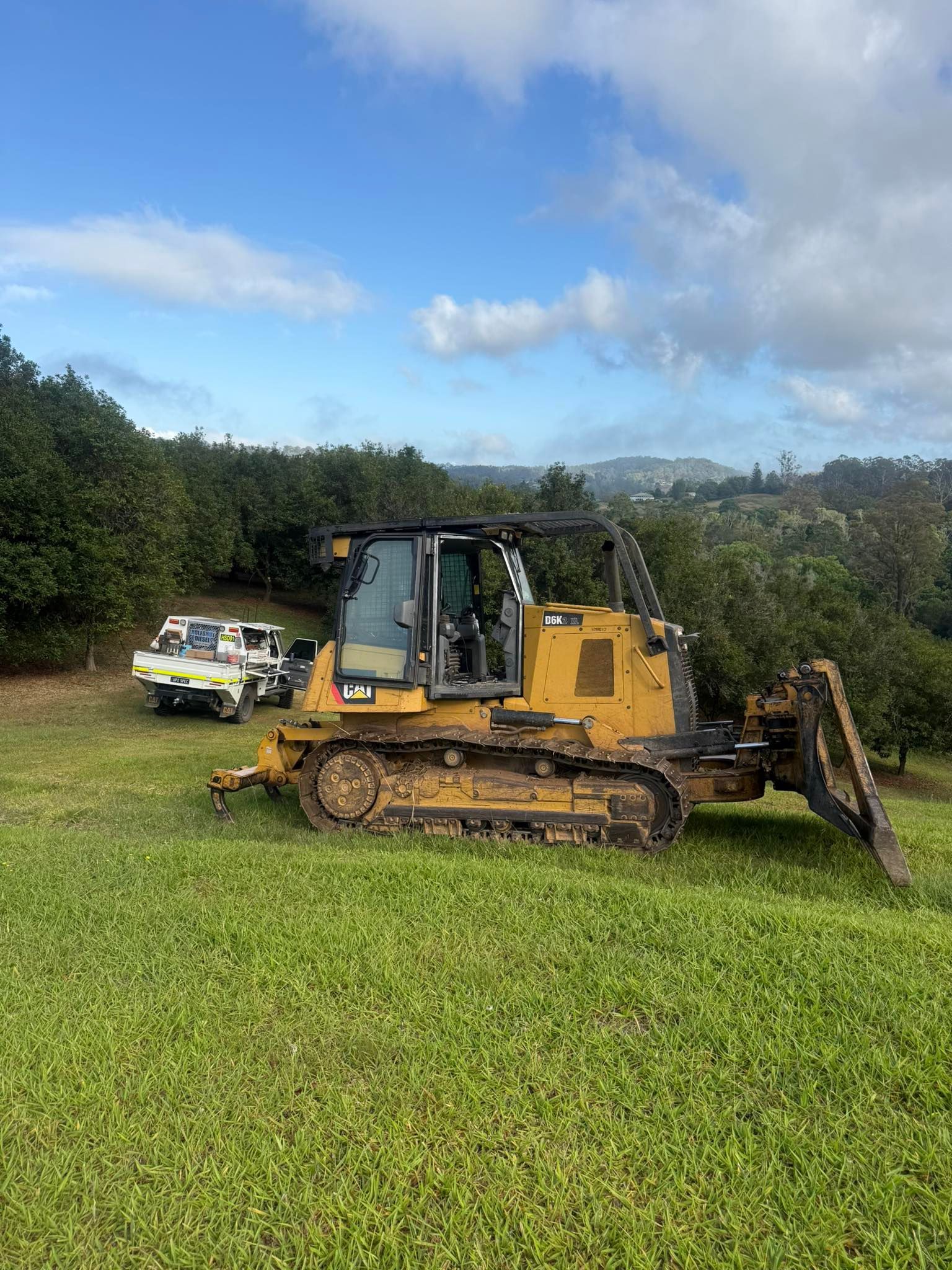Yellow Bulldozer on a Grassy Hill, With a Truck Nearby — HOLESHOT Diesel In Sunshine Coast, QLD