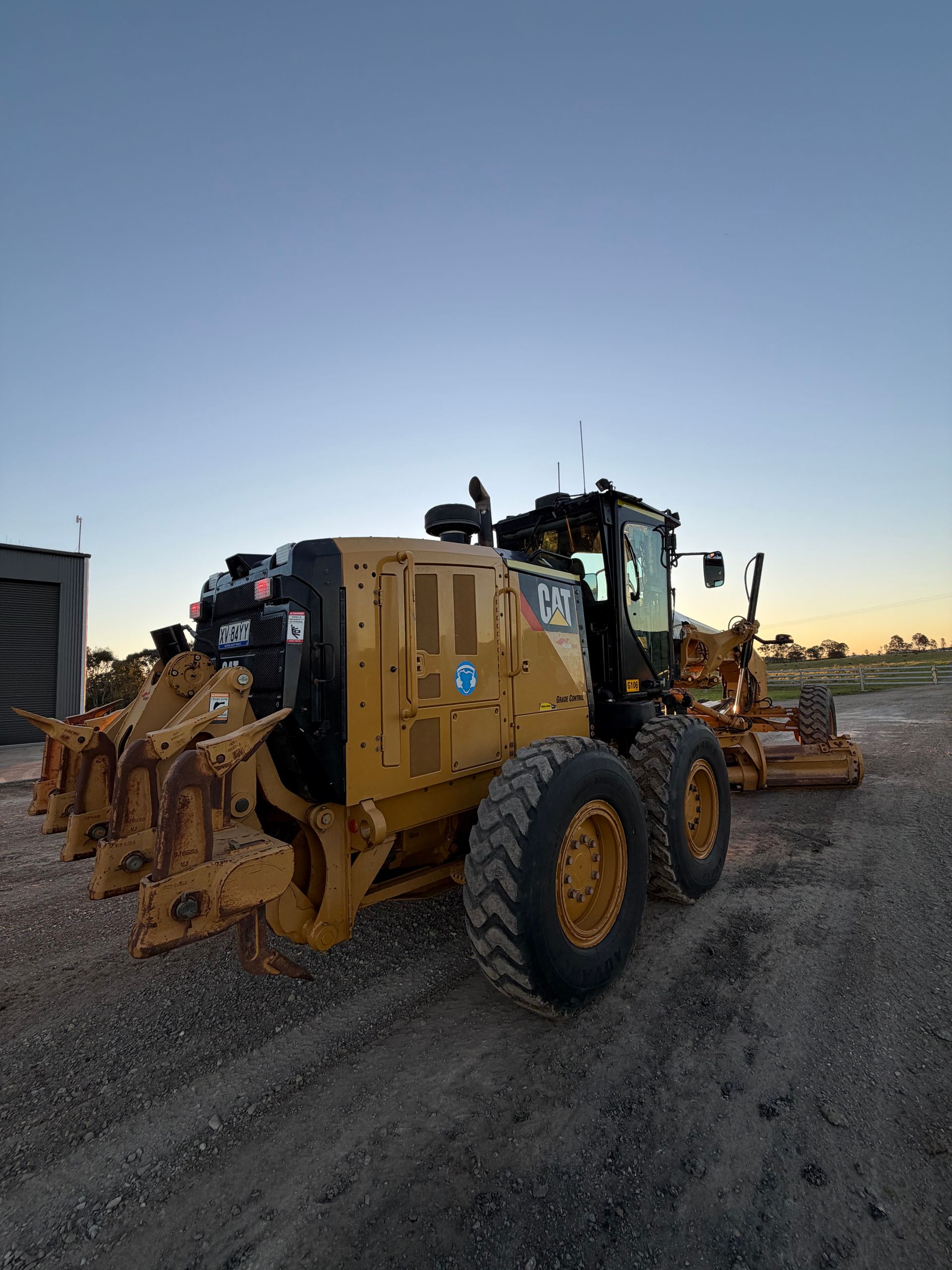 Yellow Caterpillar Grader on Gravel, With a Dusky Blue Sky — HOLESHOT Diesel In Toowoomba, QLD