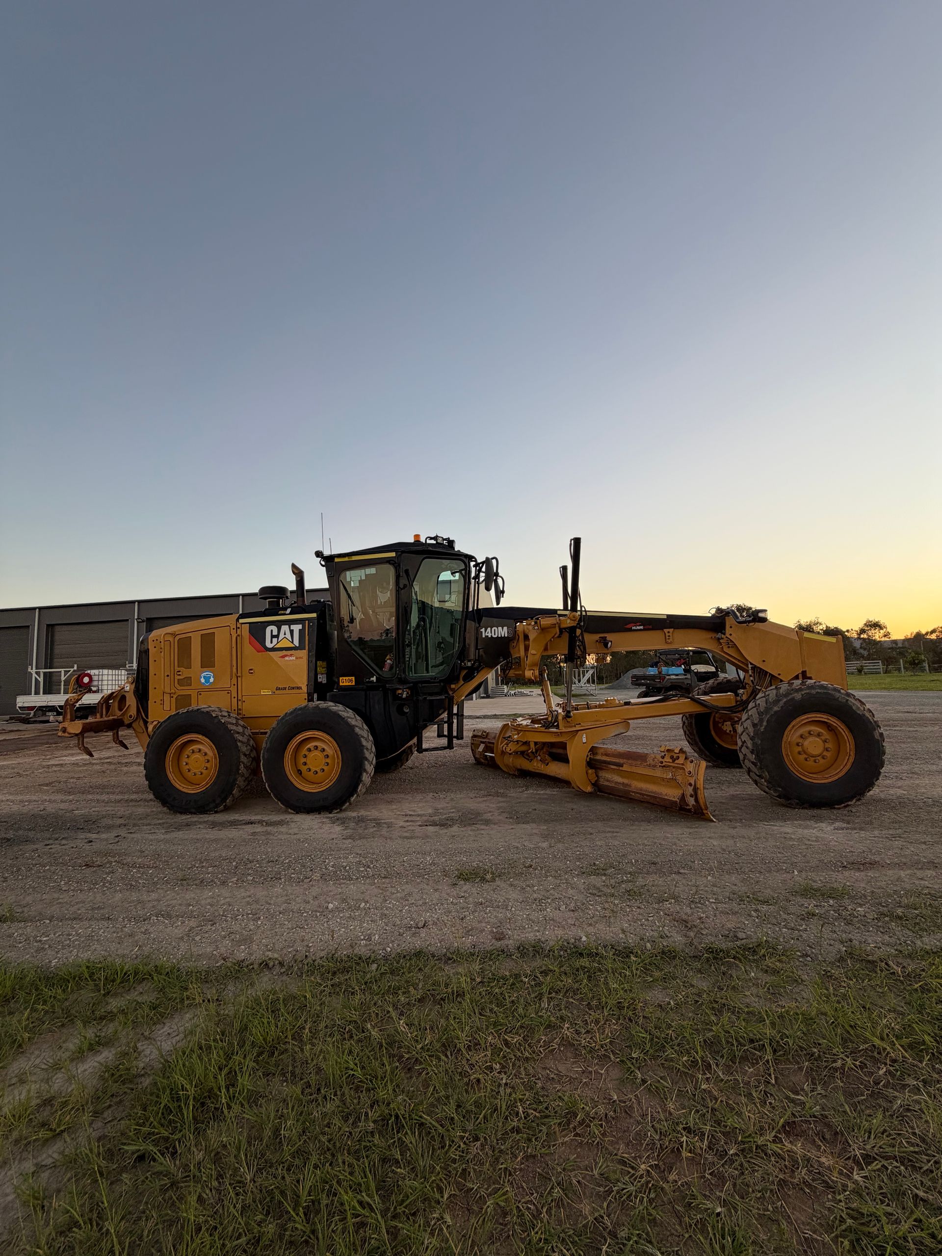 Yellow Caterpillar Motor Grader on Gravel Under a Blue Sky at Sunset — HOLESHOT Diesel In Miles, QLD