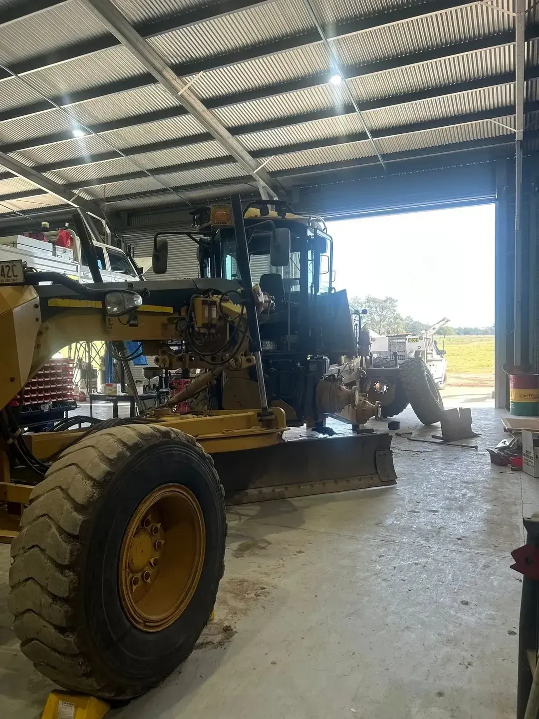 Yellow Grader Inside a Shed With an Open Door, Facing a Field — HOLESHOT Diesel In Blackwater, QLD
