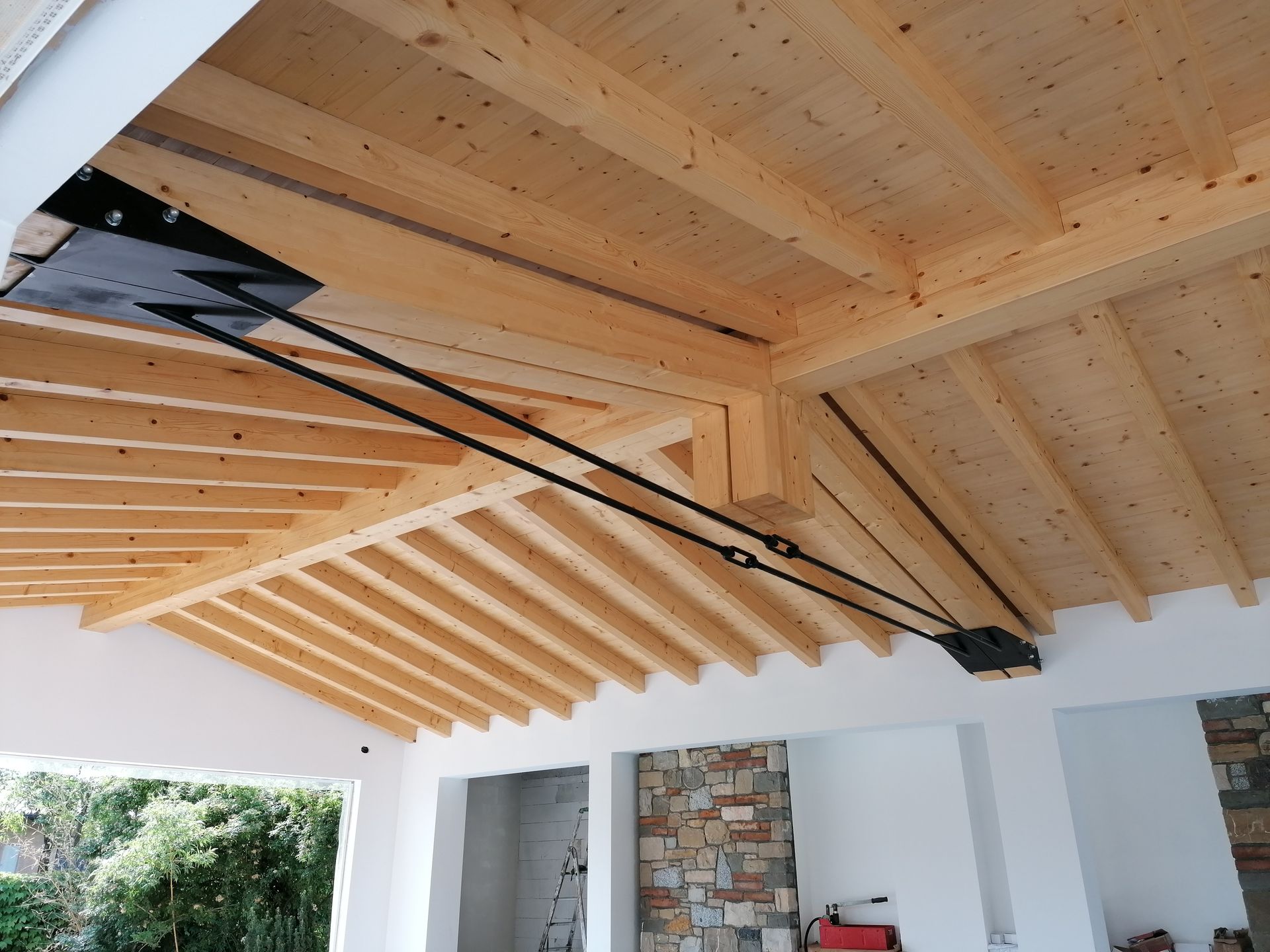 Soffitto in legno con travi di sostegno e cavi neri, parte della struttura di un edificio.