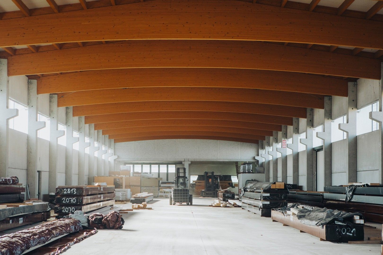 Interno di un grande magazzino con soffitto con travi in ​​legno e supporti in cemento. Materiali da costruzione visibili sul pavimento.