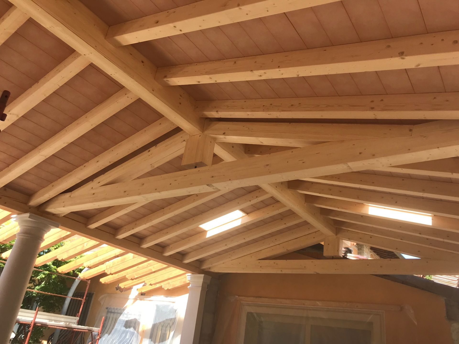 Travi e travi in ​​legno che formano la struttura del tetto, con un soffitto e pilastri color marrone chiaro visibili.