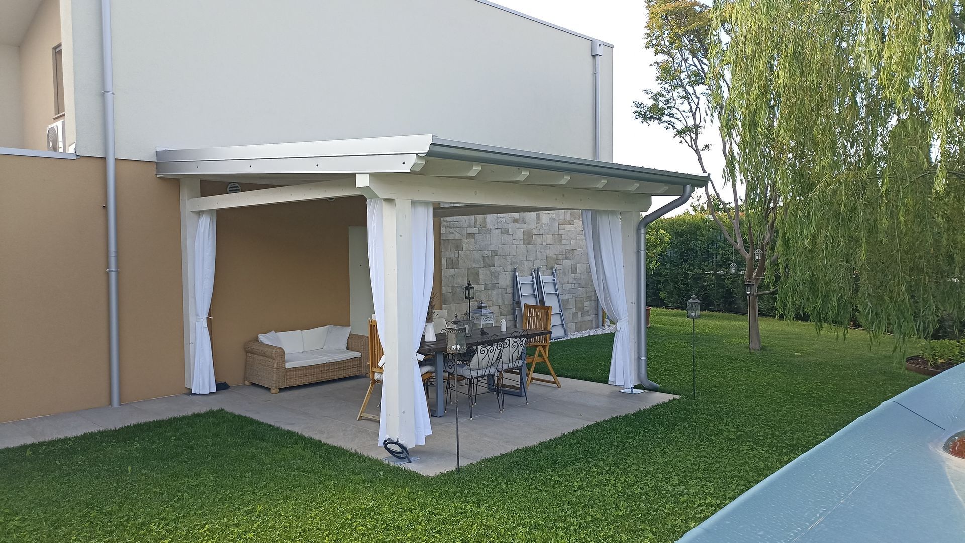 Patio coperto con tende, posti a sedere e tavolo in giardino.