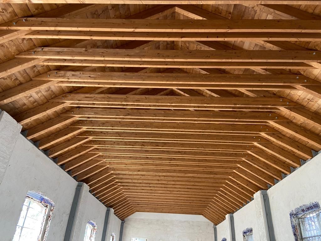 Travi in ​​legno sul soffitto in una stanza luminosa con pareti e finestre bianche.