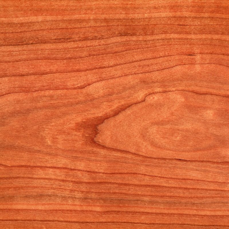 Primo piano delle venature del legno di ciliegio color rosso-marrone con motivi a spirale.