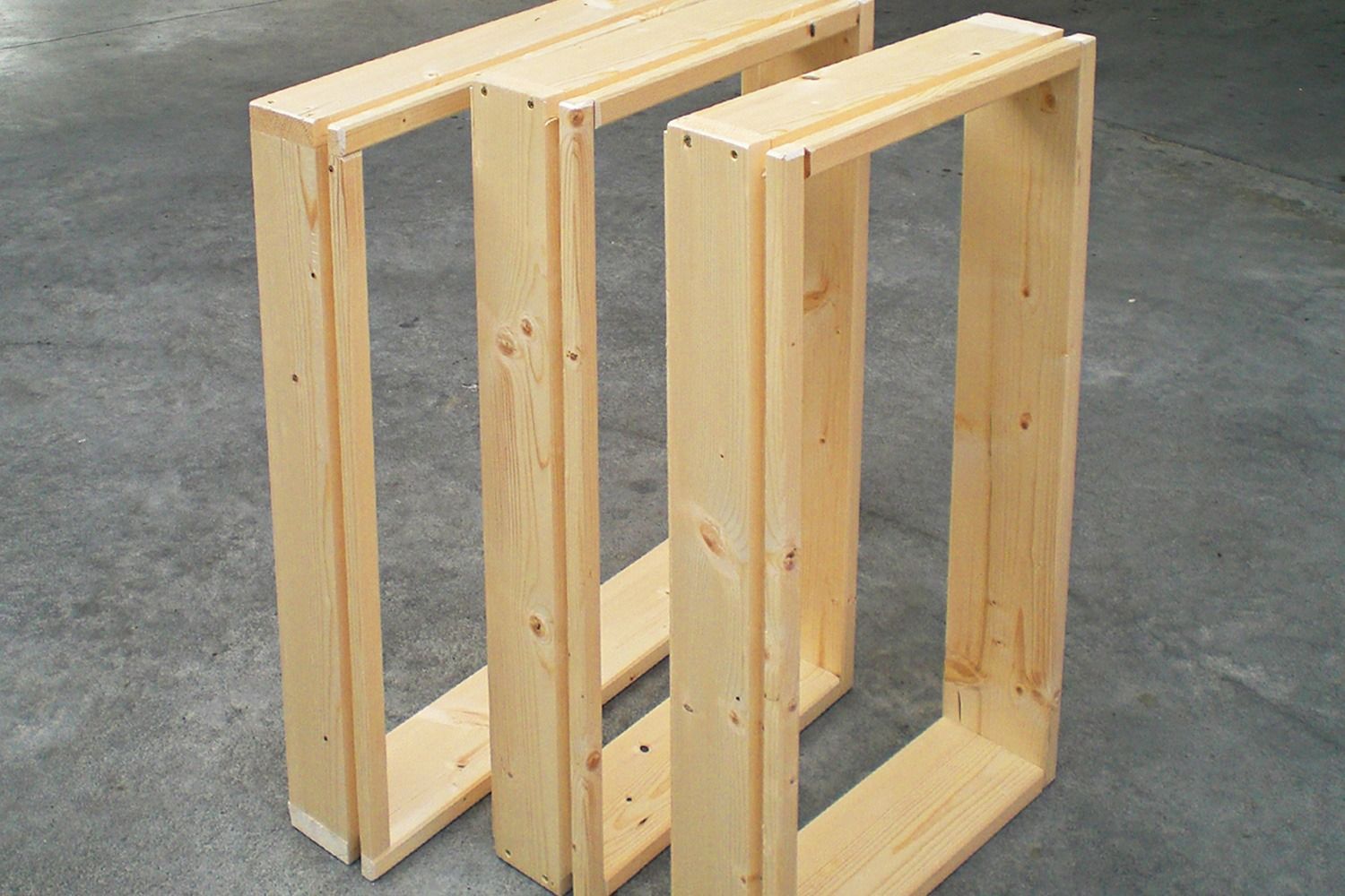 Tre telai in legno grezzo assemblati, verticali e pronti all'uso, su una superficie di cemento.