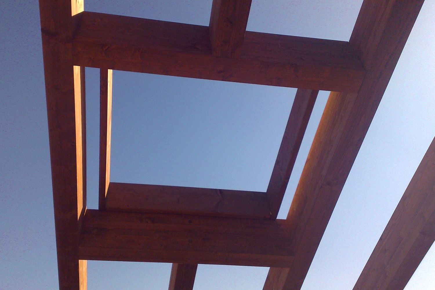 Pergola in legno con apertura quadrata contro un cielo azzurro terso.
