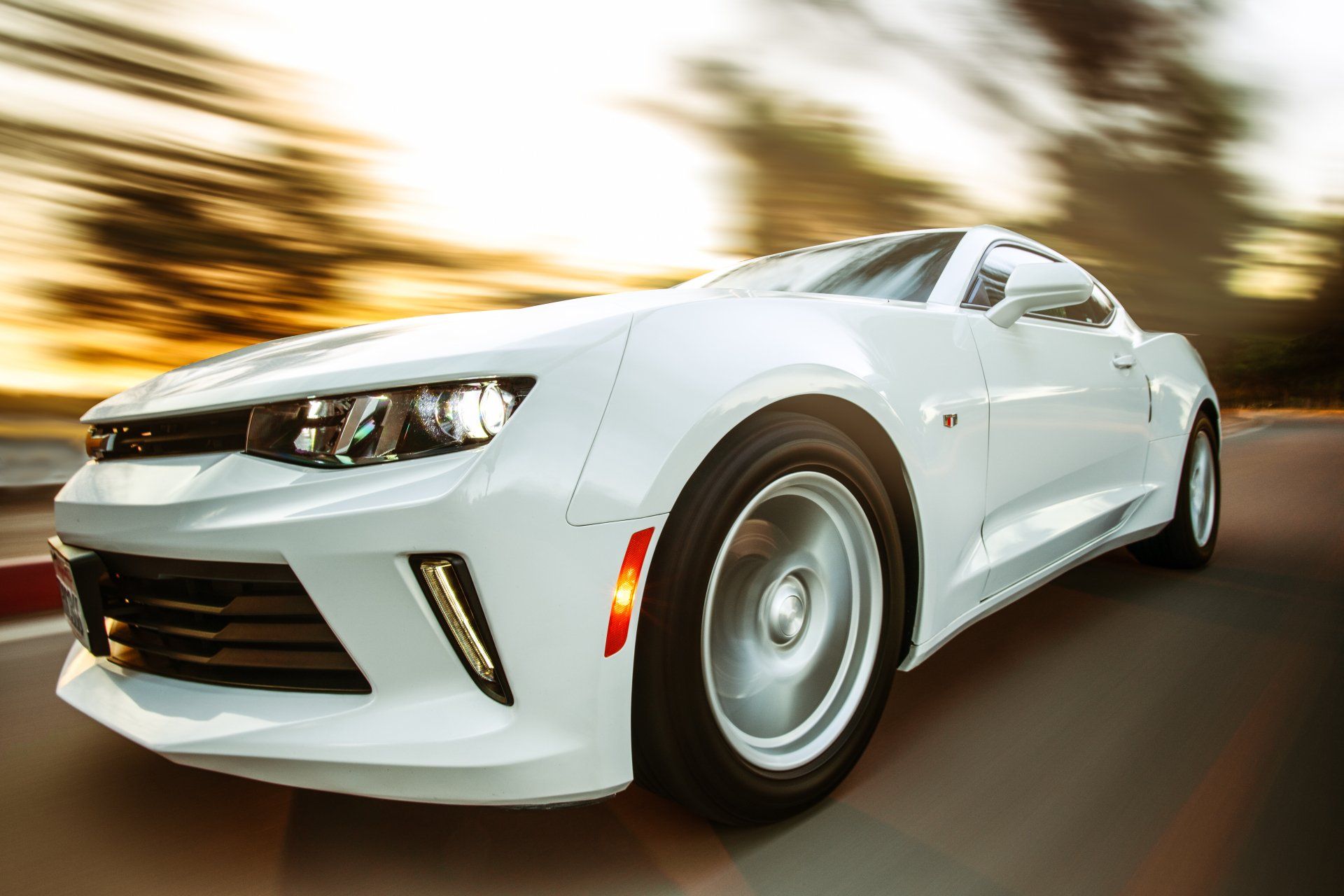 A white sports car is driving down a street at sunset.