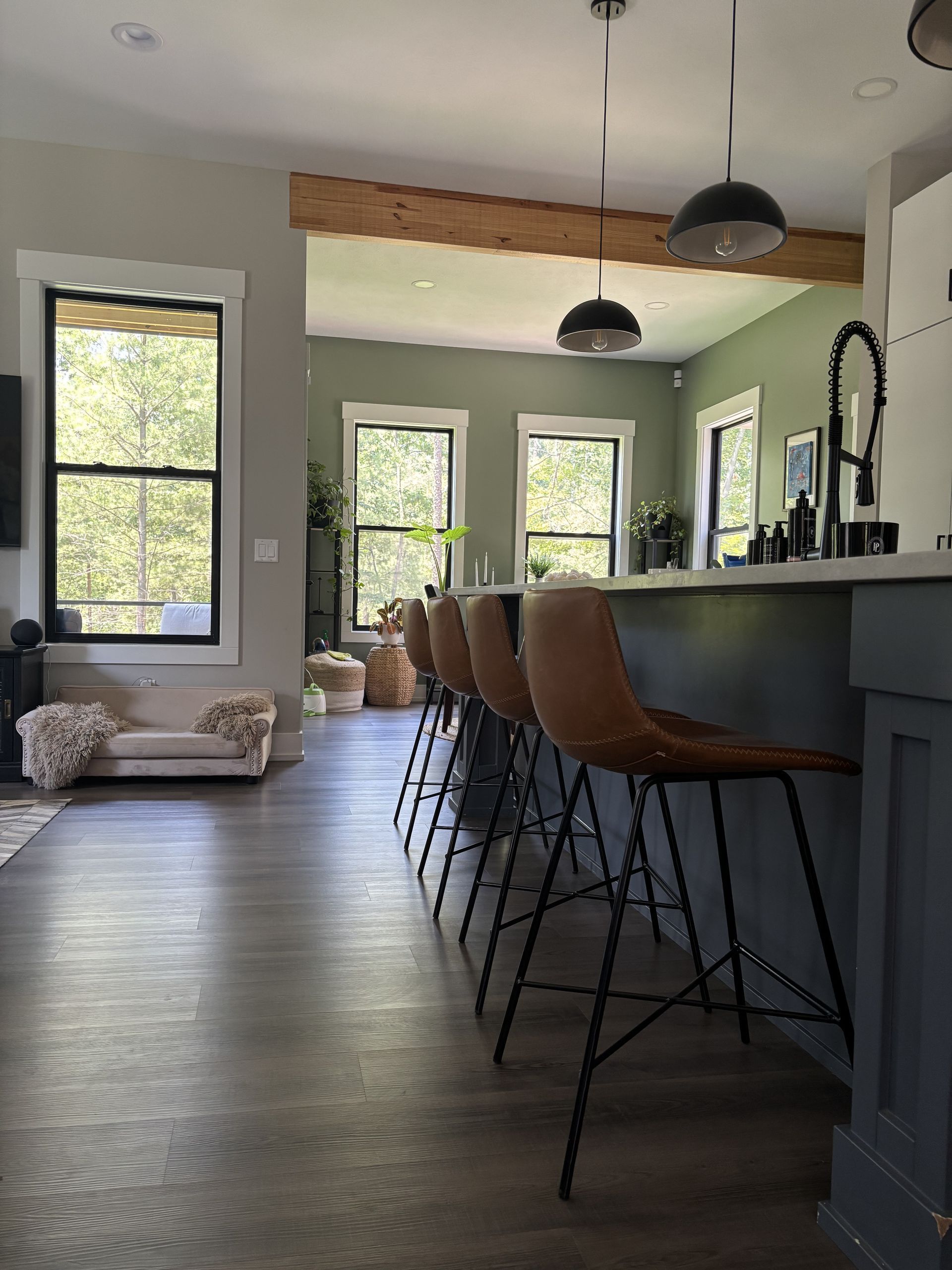 Interior kitchen view, bar stools, dark wood flooring, green walls, and wooden beams.