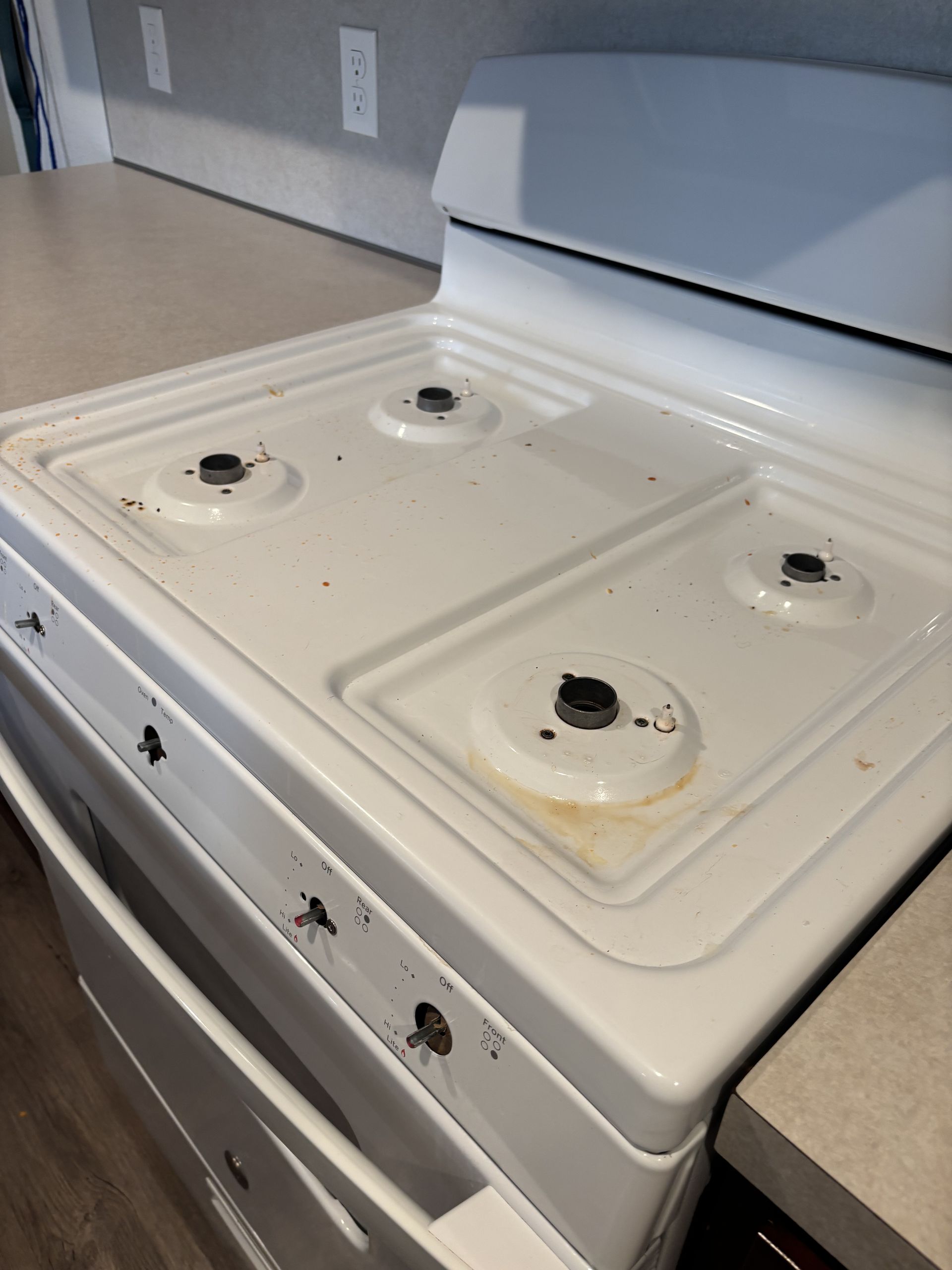 White stovetop with four burners, showing signs of use, next to a countertop.