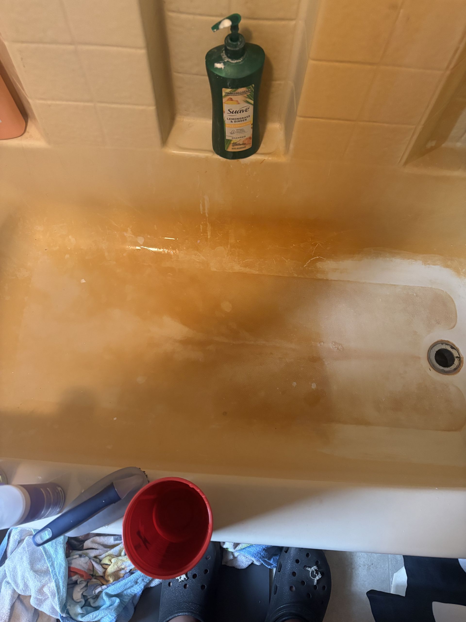 Brown-stained bathtub with cleaner being sprayed.  A green soap bottle sits in a niche.