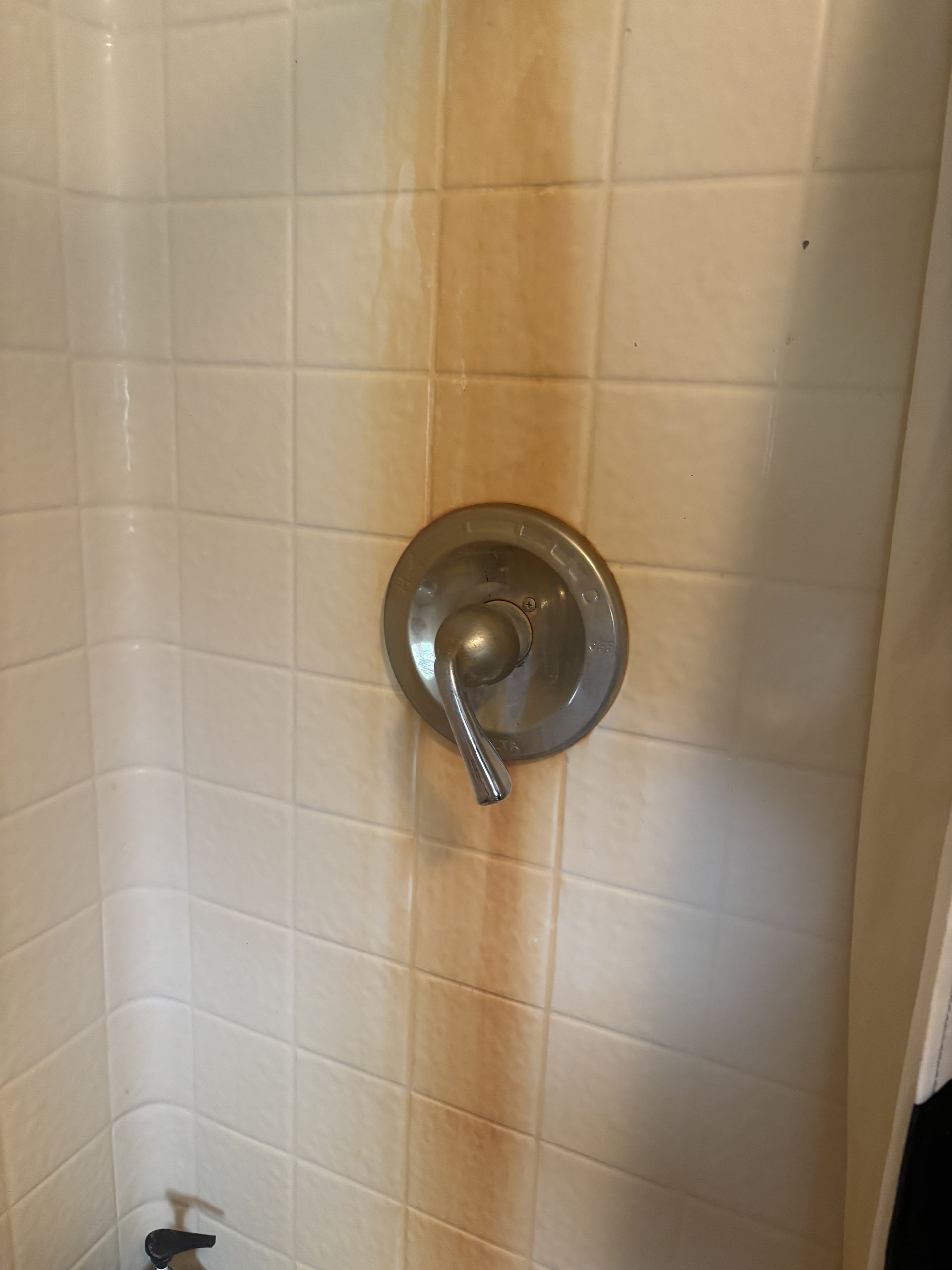 Rust stains on white tiled shower wall with faucet.