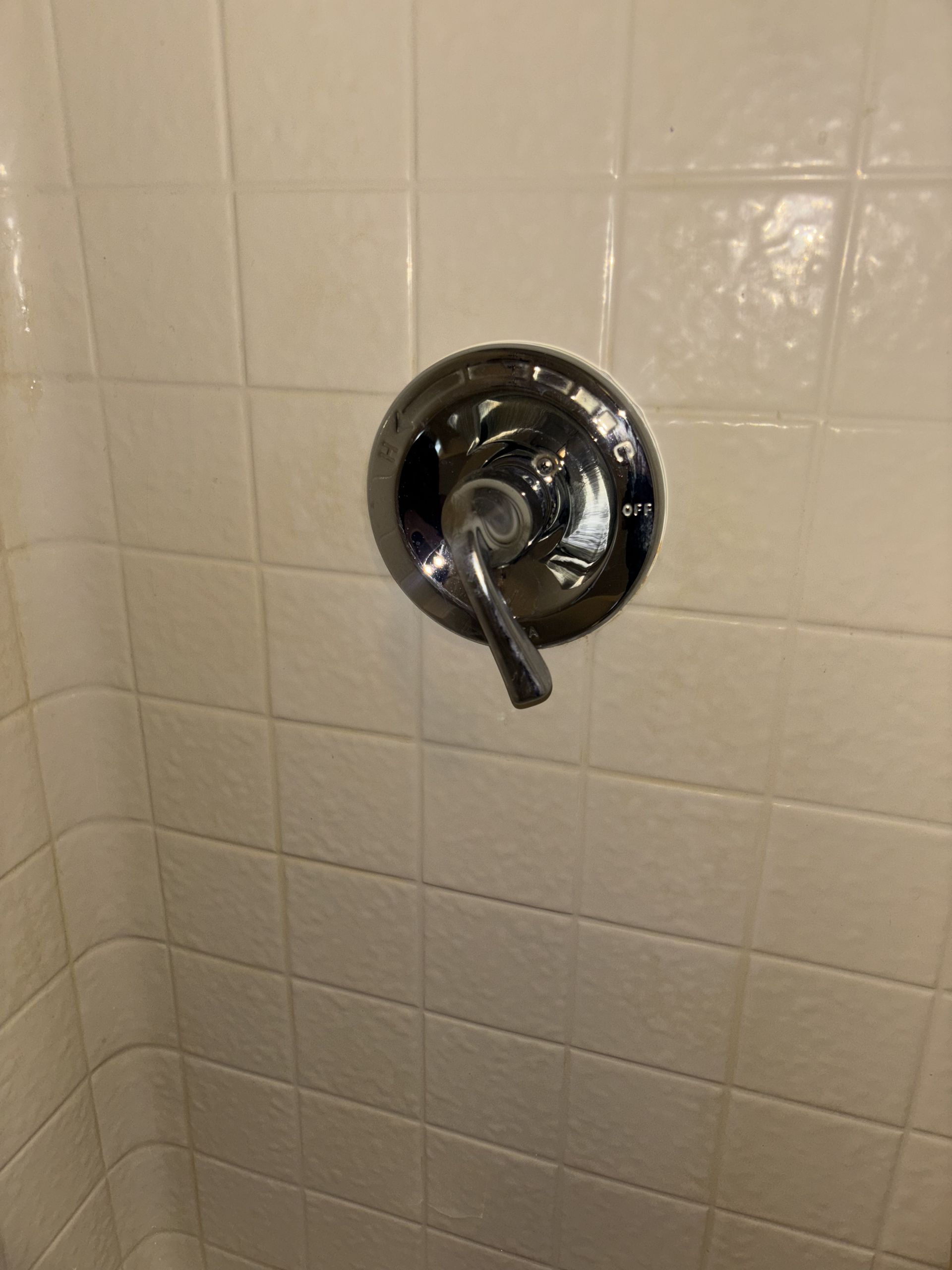 Chrome shower faucet with lever on white tile wall.