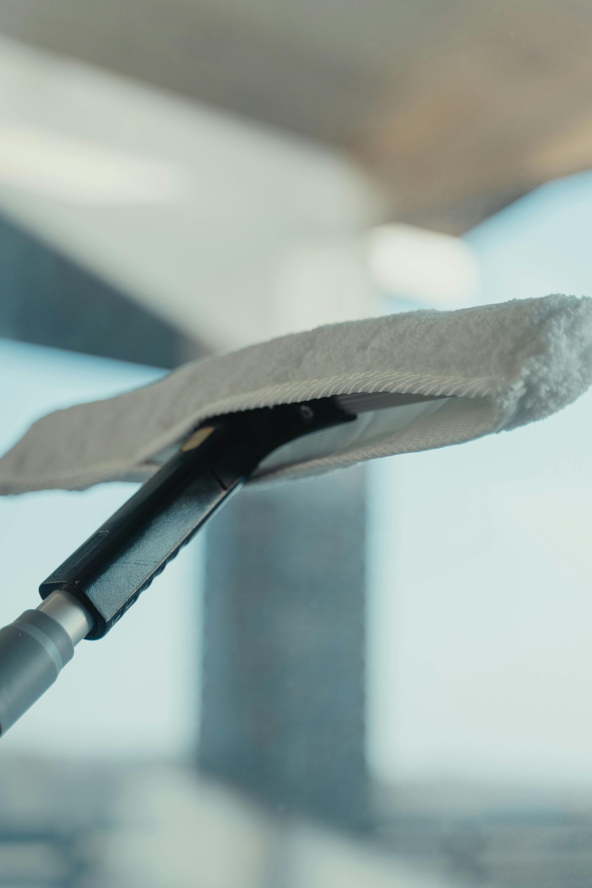 A white microfiber window cleaning tool with a black handle cleans a window.