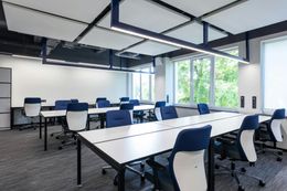 Modern office with rows of white desks, blue chairs, and sound-dampening ceiling panels.