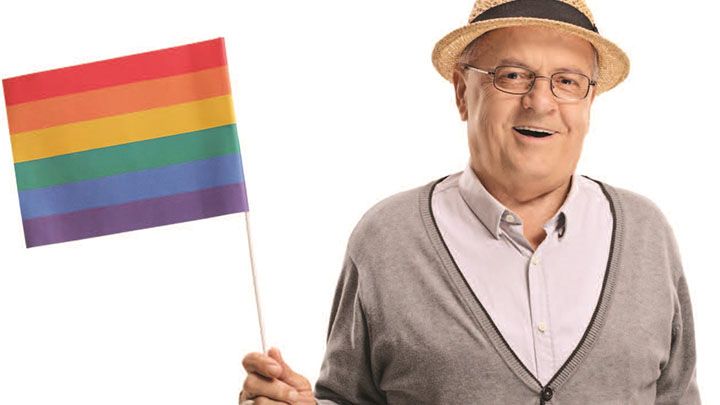 An elderly man in a hat is holding a small rainbow flag.