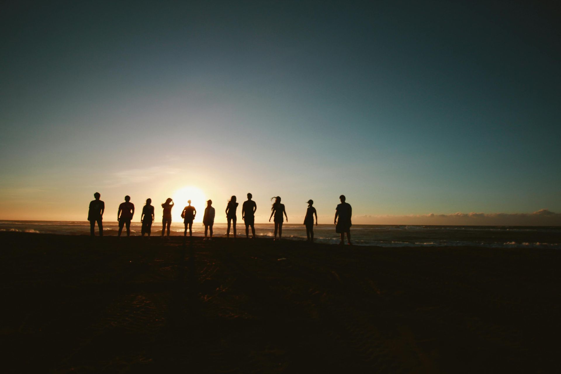 A group of people are standing in a row on a beach at sunset.