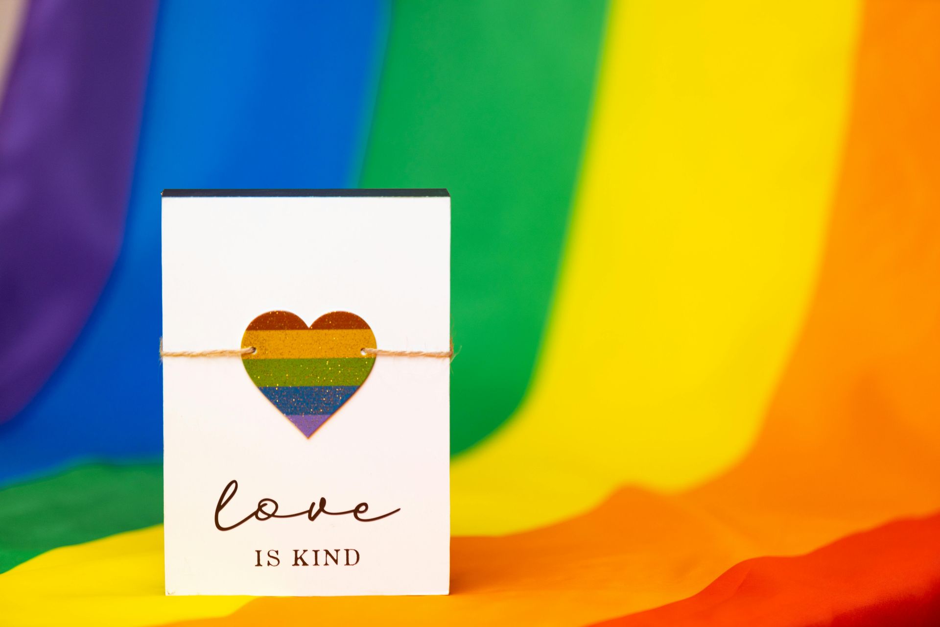 A card with a rainbow heart on it is sitting in front of a rainbow flag.