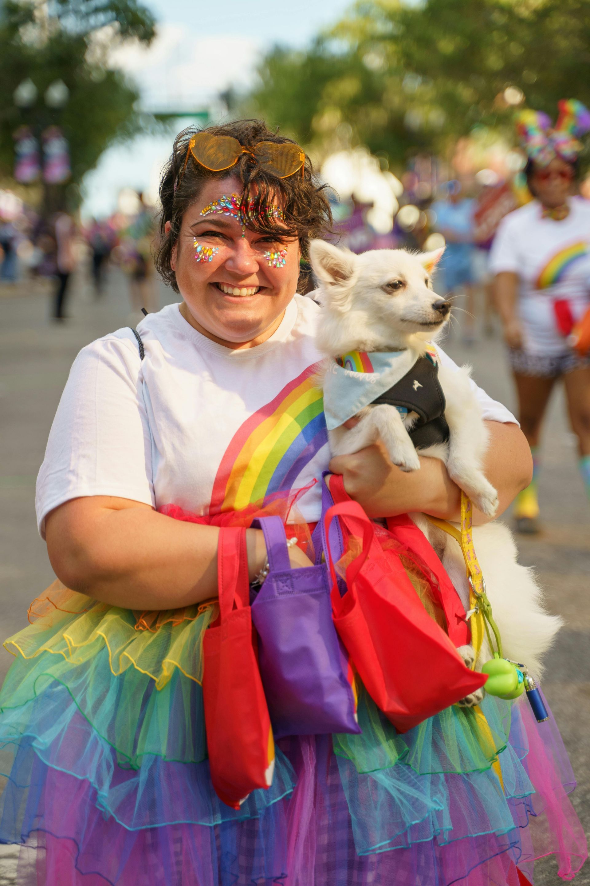 A woman in a rainbow dress is holding a small white dog.