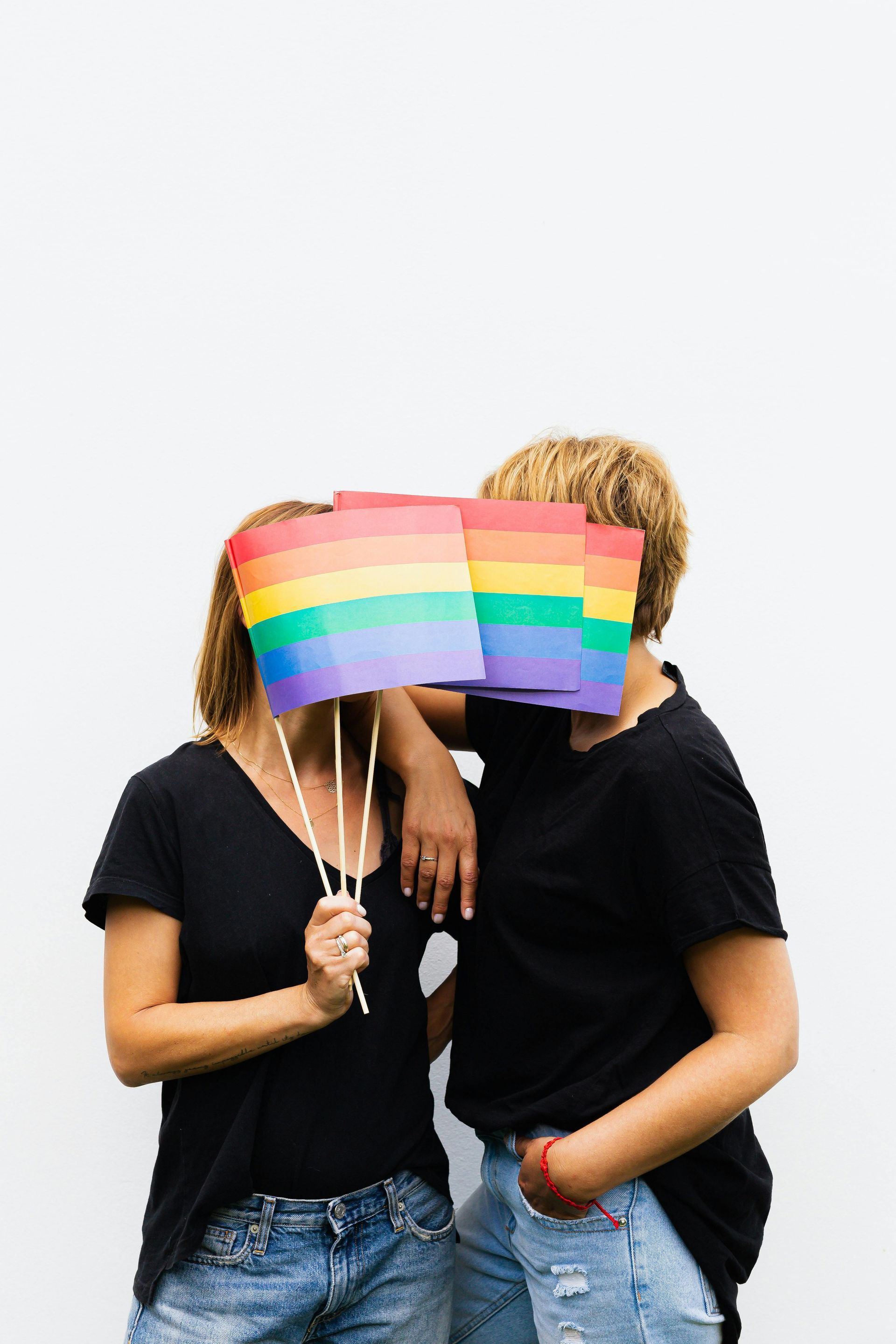 A man and a woman are holding a rainbow flag in front of their faces.