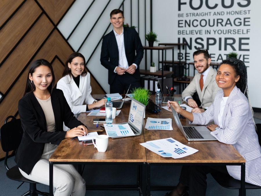 A group of people are sitting around a table with laptops.